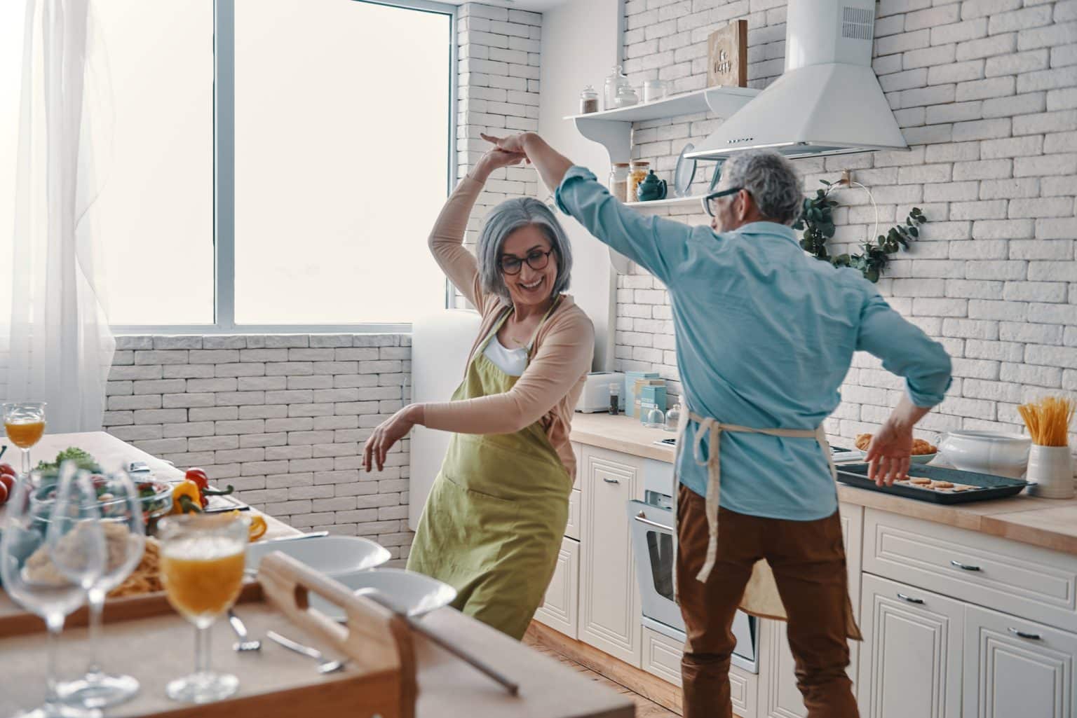 couple treating hearing loss with implants Older woman and her husband dancing in the kitchen while preparing dinner.